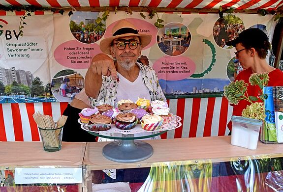 Zwei Personen stehen hinter einem Stand mit bunten Cupcakes und Informationen zur Gropiusstädter Bewohnervertretung auf einem Nachbarschaftsfest.