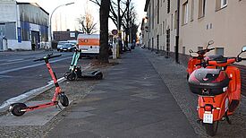 E-Roller und ein Mofa stehen auf einem Gehweg und stellen für die Menschen im Kiez ein Hindernis dar. 