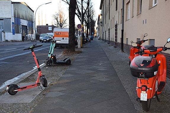 E-Roller und ein Mofa stehen auf einem Gehweg und stellen für die Menschen im Kiez ein Hindernis dar. 