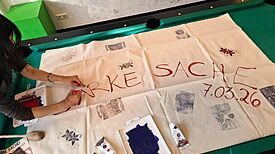 Eine Person bemalt ein großes Tuch auf einem Billardtisch mit dem Schriftzug „Starke Sache“.