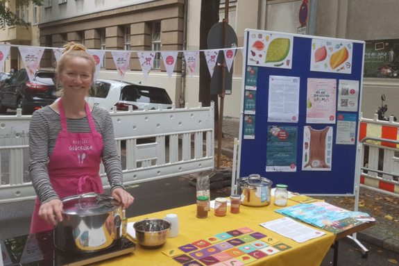 Eine Frau mit Schürze steht hinter einem Kochtopf und lächelt in die Kamera