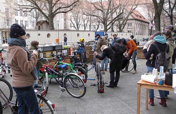 Menschen versammeln sich mit Fahrrädern im Kiezgarten, während einige ihre Räder reparieren lassen.