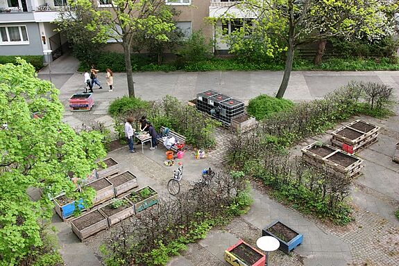 Luftaufnahme eines Gemeinschaftsgartens mit Hochbeeten und Menschen, die im Garten arbeiten.