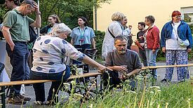 Mehrere Menschen stehen und sitzen an einer bepflanzten Fläche und schauen auf die Pflanzen.