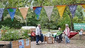 Mehrere Menschen sitzen auf Stühlen im Gemeinschaftsgarten. 