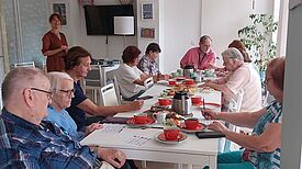 Eine Gruppe von Seniorinnen und Senioren sitzt um einen Tisch und spielt Bingo. 