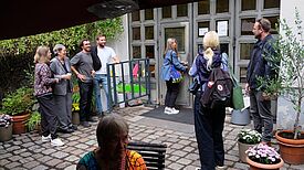 Mehrere Menschen stehen und unterhalten sich vor dem Eingang des Zentrums Gitschiner 15, eine Frau öffnet gerade die Tür zum Gebäude.