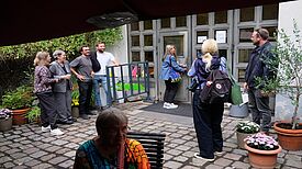 Mehrere Menschen stehen und unterhalten sich vor dem Eingang des Zentrums Gitschiner 15, eine Frau öffnet gerade die Tür zum Gebäude.