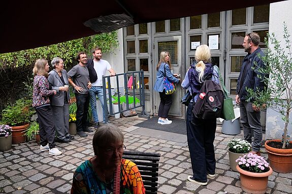 Mehrere Menschen stehen und unterhalten sich vor dem Eingang des Zentrums Gitschiner 15, eine Frau öffnet gerade die Tür zum Gebäude.