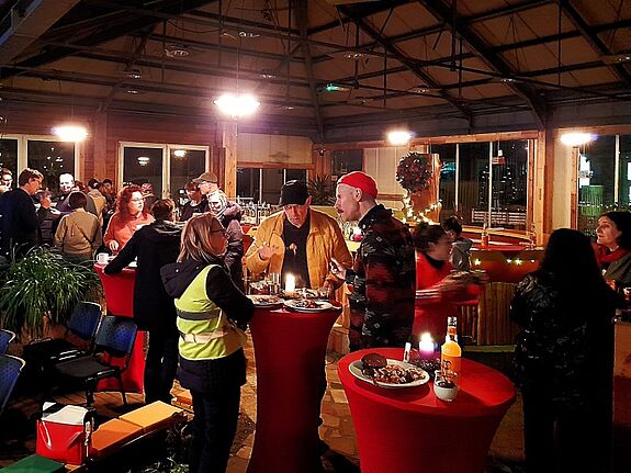 Menschen stehen an Tischen zusammen, essen und reden miteinander. 