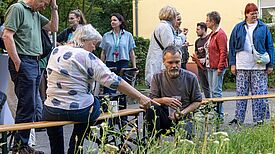 Mehrere Menschen stehen und sitzen an einer bepflanzten Fläche und schauen auf die Pflanzen.