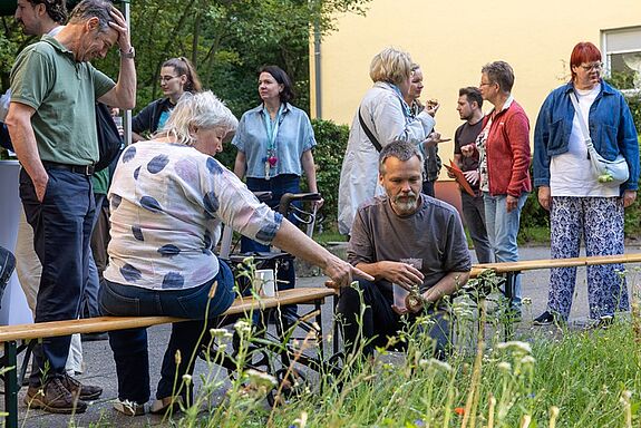 Mehrere Menschen stehen und sitzen an einer bepflanzten Fläche und schauen auf die Pflanzen.