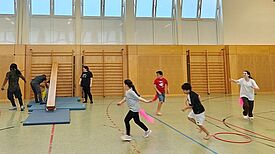 Kinder und Erwachsene rennen gemeinsam durch eine Sporthalle. 