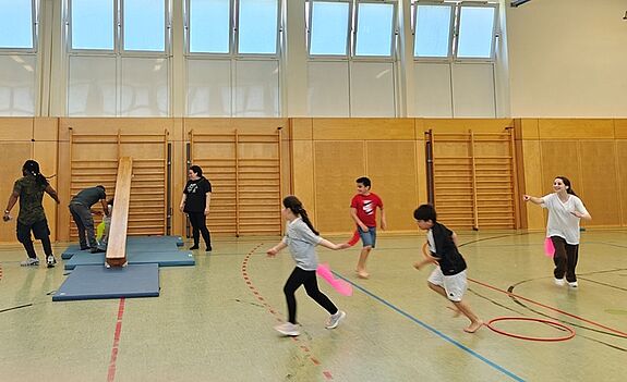 Kinder und Erwachsene rennen gemeinsam durch eine Sporthalle. 