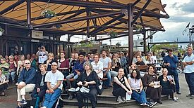Viele Engagierte sitzen und stehen auf dem Parkdeck des Klunkerkranichs unter einem großen Sonnensegel und nehmen am Sommerfest teil. 