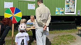 Kinder und Eltern stehen vor dem Bauwagen an einem Glücksrad-Stand von Schwarz-Weiß Spandau im Falkenhagener Feld.