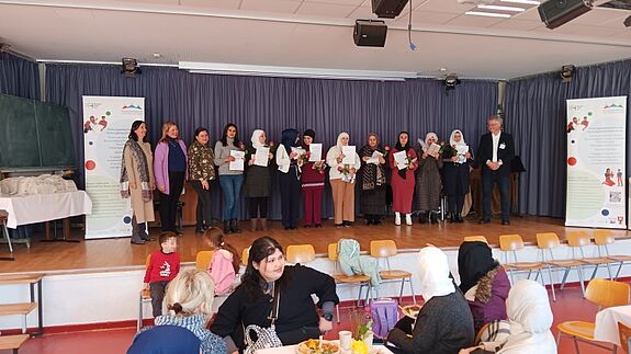Alle neun neuen Bildungsbotschafterinnen stehen mit der Bezirksstadträtin Eva Majewski und dem Projektteam um Henriette Harms, Britta Seidl und Heinz Bruland in der Nahariya-Schule auf der Bühne.