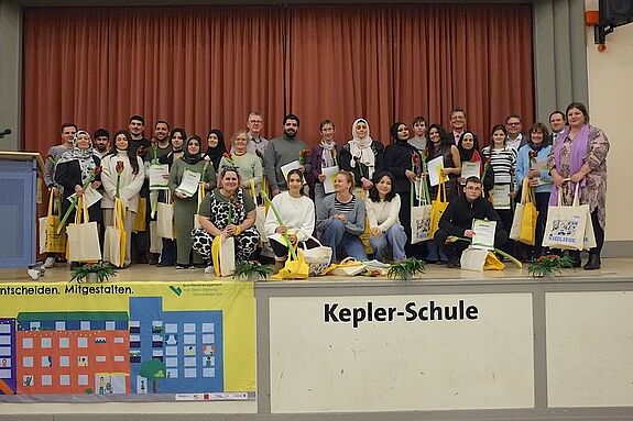 Die Ehrenamtlichen versammeln sich mit Urkunden und Geschenken auf der Bühne der Kepler-Schule.