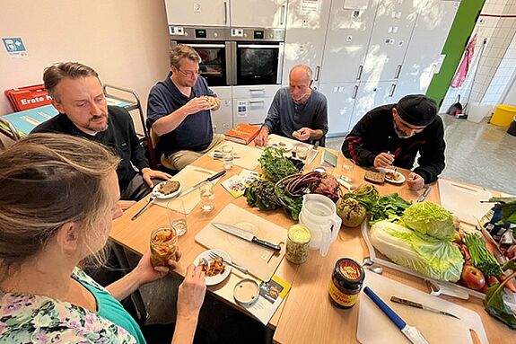 Fünf Teilnehmende kosten am Küchentisch das selbstgemachte Kimchi und fermentierte Gemüse.