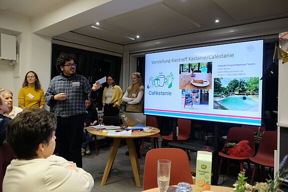 Menschen hören einem Mann zu, der vor einer Präsentationswand steht.