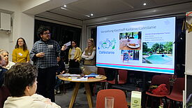 Menschen hören einem Mann zu, der vor einer Präsentationswand steht.