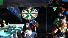 Kinder stehen vor einer Drehscheibe an einem Info-Stand auf dem Kiezfest in der Thermometersiedlung.  
