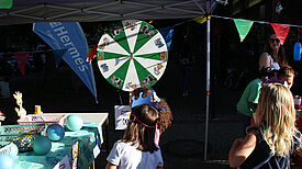 Kinder stehen vor einer Drehscheibe an einem Info-Stand auf dem Kiezfest in der Thermometersiedlung.  
