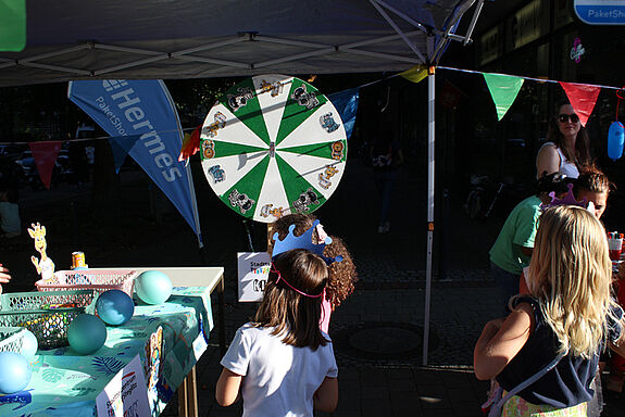 Kinder stehen vor einer Drehscheibe an einem Info-Stand auf dem Kiezfest in der Thermometersiedlung.  