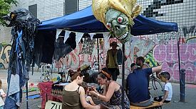 Zwei Kinder werden an einem bunt geschmückten Stand geschminkt.