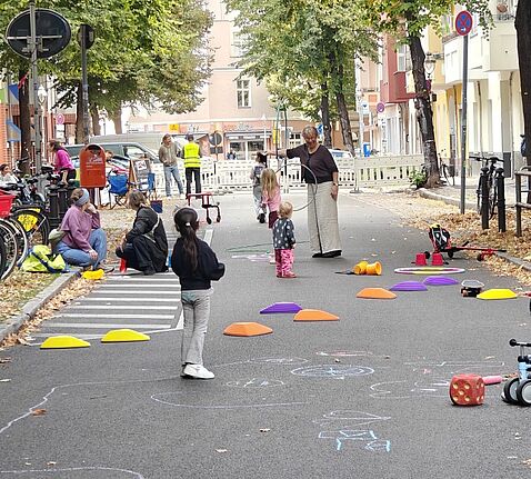 Kinder und Erwachsene spielen auf einer abgesperrten Straße mit Reifen und bunten Parcourssteinen.