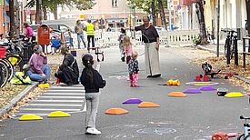 Kinder und Erwachsene spielen auf einer abgesperrten Straße mit Reifen und bunten Parcourssteinen.