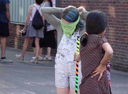 Zwei Mädchen, davon eines mit verbundenen Augen, spielen. 