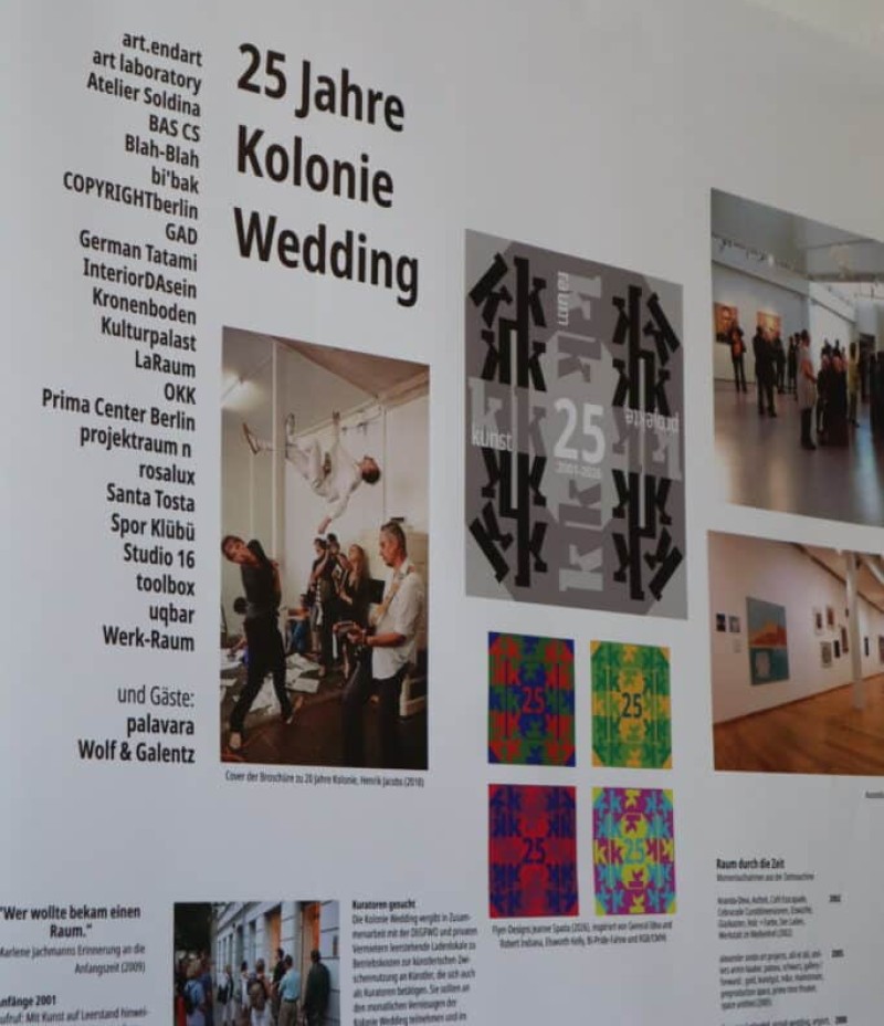 Ausstellungstafel zu 25 Jahren Kolonie Wedding mit Fotos, Plakaten und Texten in einem Projektraum.
