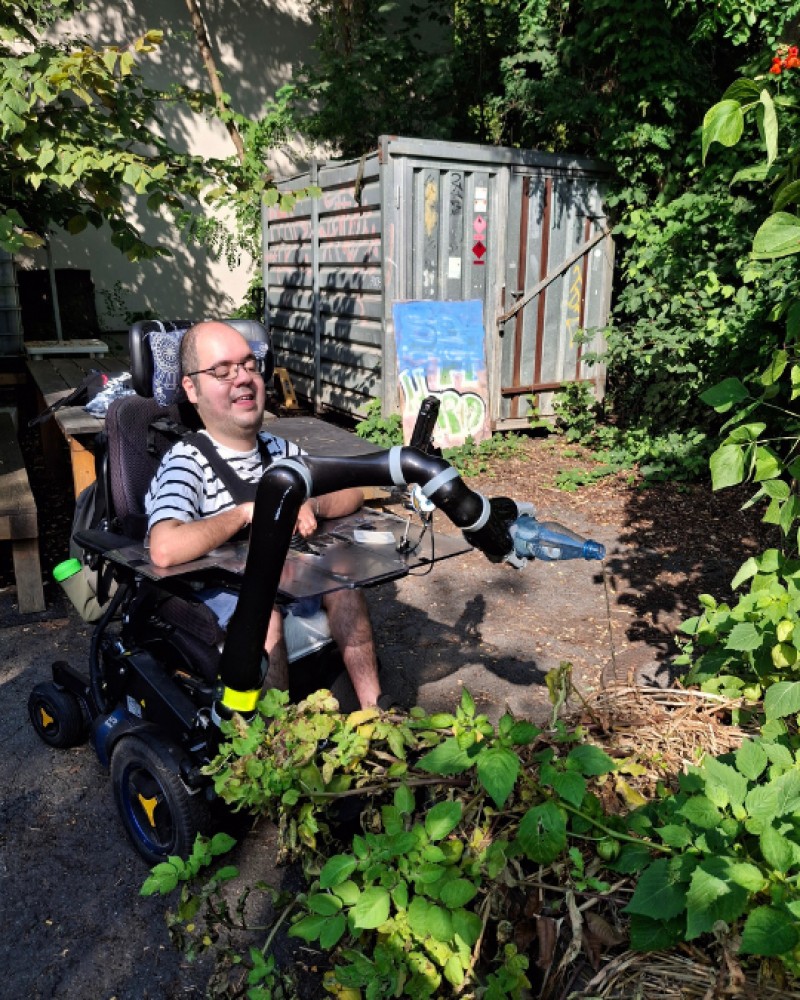 Eine Person im Rollstuhl gießt mit Greifarm Pflanzen im Gemeinschaftsgarten Rollberg Paradise.