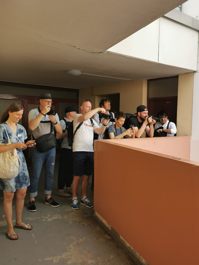 Mehrere Personen stehen auf einem offenen Hausflur und machen Fotos. 