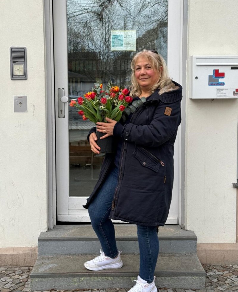 Sidika Özdemir, die ehrenamtlich den Frauentreff organisiert, steht vor einer Tür und hält Blumen.