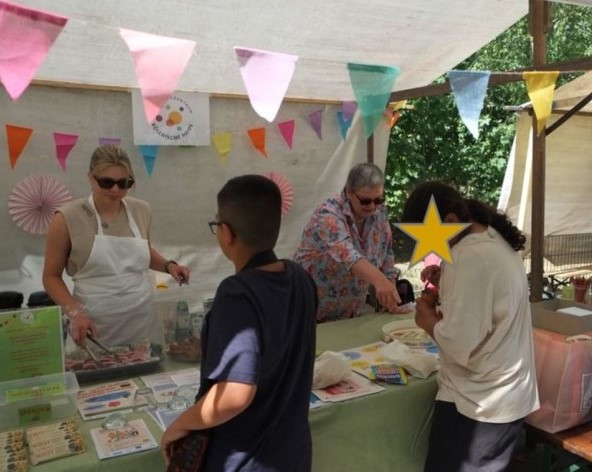 Zwei Frauen betreuen einen bunten Infostand auf einem Fest und sprechen mit Kindern.