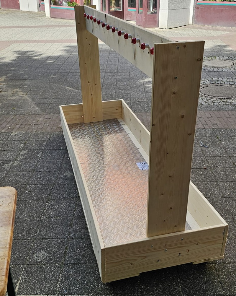Ein mobiler Kleiderständer aus Holz und mit Rollen steht auf dem Asphalt. 