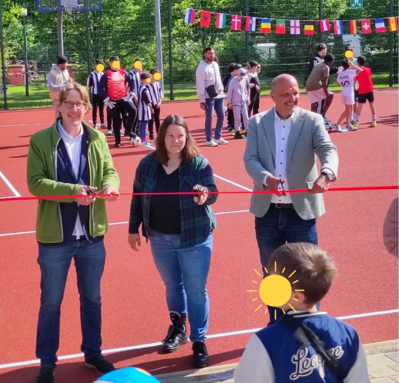 Vertretende aus Politik und Verwaltung durchschneiden gemeinsam ein rotes Band zur Eröffnung der neuen Sportanlagen der KJFE Lessinghöhe.
