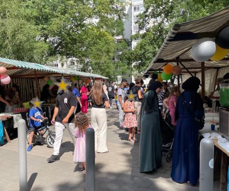 Menschen schlendern bei sonnigem Wetter an Ständen mit Ballondekorationen auf dem outreach-Sommerfest in der Dammwegsiedlung.