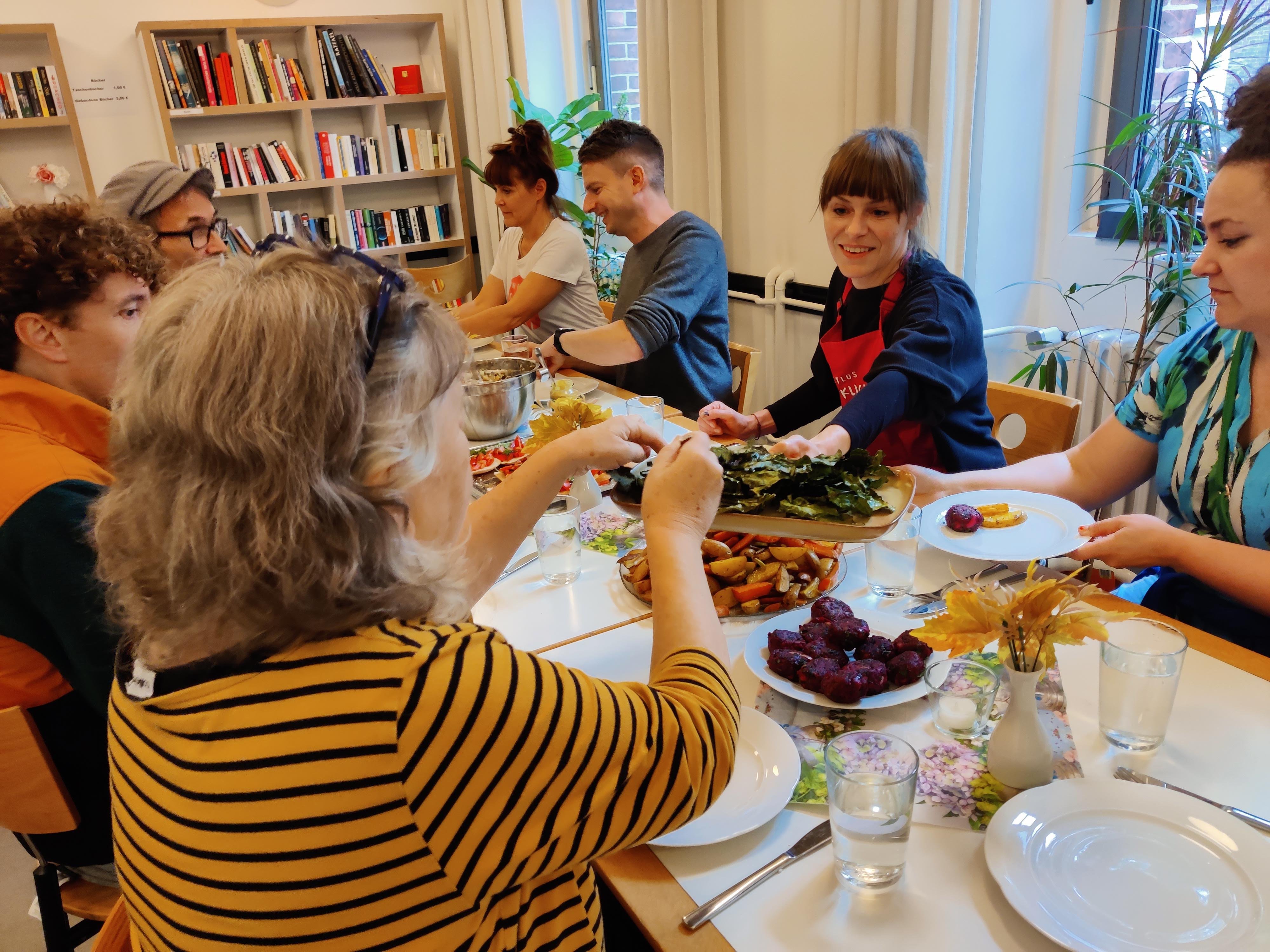 Verschiedene Personen am Tisch teilen das gemeinsam gekochte Essen und jeder tut sich von allem auf.