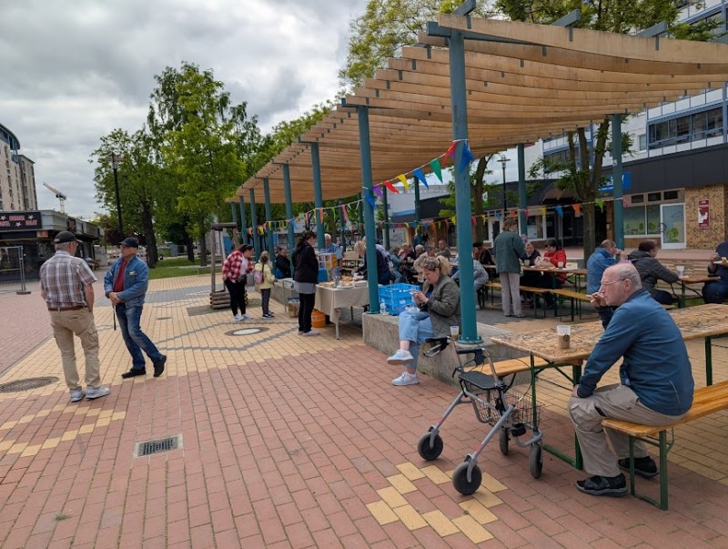 Menschen sitzen und stehen bei einem Nachbarschaftsfest auf dem Quartiersplatz im Kosmosviertel.