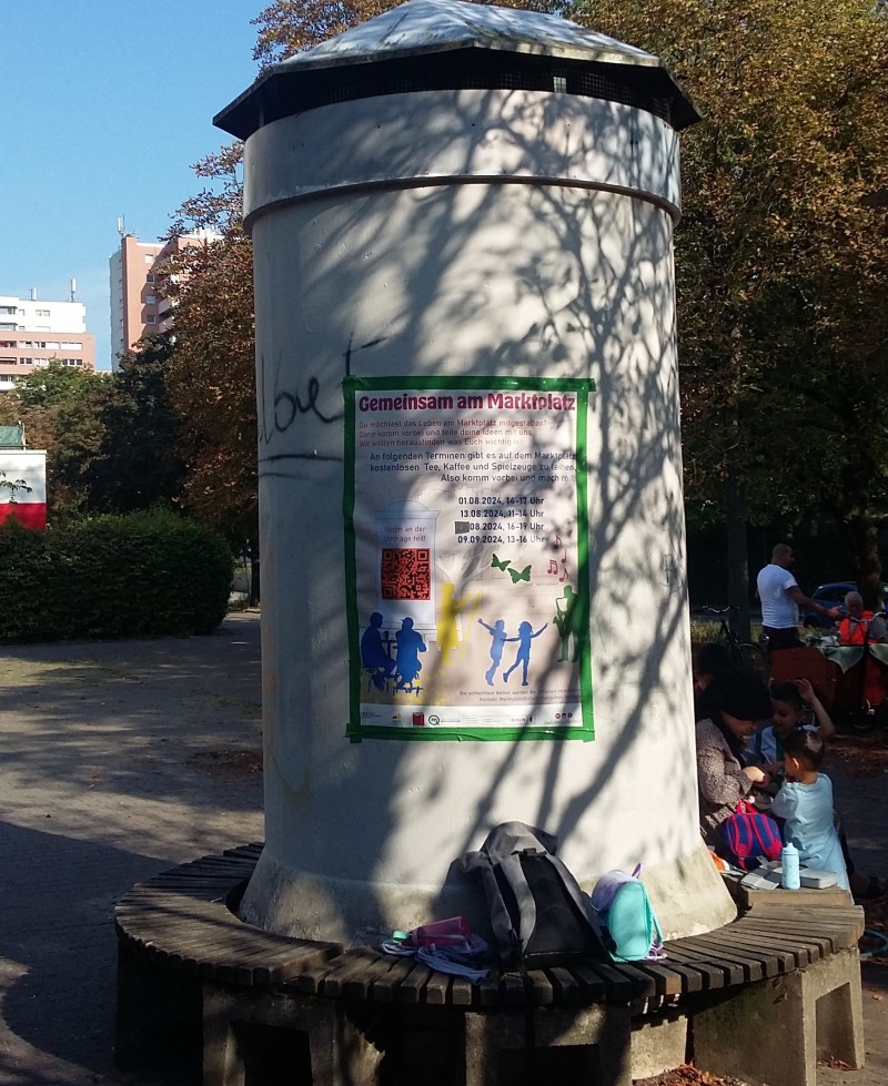 Ein Plakat mit Informationen zum Projekt „Gemeinsam am Marktplatz“ ist an einer Litfaßsäule im Quartier angebracht.