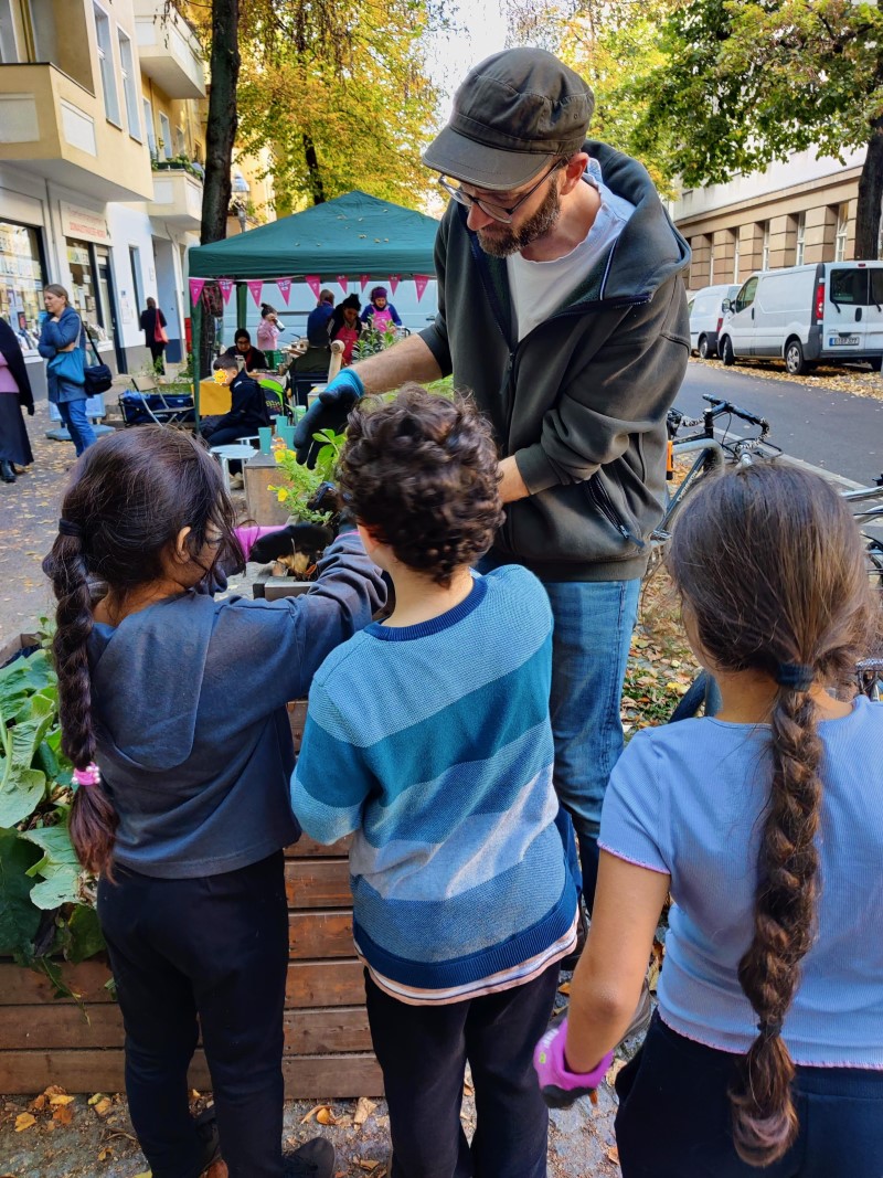 Kinder und ein Erwachsener arbeiten gemeinsam im Kiezgarten, um Pflanzen für den Winter vorzubereiten.